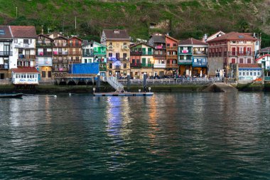 Canlı renklerle boyanmış konutlar, deniz kıyısında parıldayan yansımaları, huzurlu atmosferin tadını çıkarmak için toplanan insanlar. Pasajes San Juan, İspanya, Bask ülkesi..
