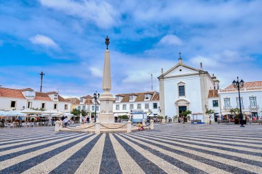 Canlı bir kasaba meydanında geleneksel beyaz binalar ve canlı kafelerle çevrili çarpıcı bir dikilitaş bulunur. Vila Real de Santo Antonio, Portekiz