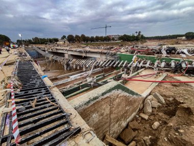 Yeniden yapılanma çabaları hasar görmüş bir köprü alanını ortaya çıkararak, kent manzarasında meydana gelen yakın tarihli bir felaketten kaynaklanan kaos ve yıkımın altını çiziyor. İşçiler enkazı ve yıkık yapıları değerlendiriyor. Paiporta, Dana, Valencia, İspanya.