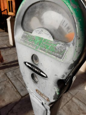 Bir parkmetre yaşını ve yıpranmasını gösterir, soluk detaylar ve görünür bir sınırlayıcı içerir. Güneş ışığı, kentsel bir çevrede hareketli bir kaldırım boyunca varlığını vurgular.