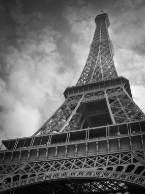 Ziyaretçiler Eiffel Kulesi 'ne hayranlıkla bakıyor, demir kafes ayrıntıları Paris' in kalbinde dramatik bulutlu bir zemin üzerine güzel vurgulanıyor..