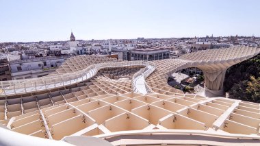 Seville üzerinde çarpıcı ahşap bir yapı beliriyor, modern tasarım ile tarihi ufuk çizgisini harmanlıyor. Güneş parıldıyor, aşağıdaki eşsiz şekilleri ve hareketli şehri aydınlatıyor..