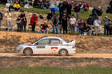 Mitsubishi Lancer Evo 'nun ralli arabası toprak yolda hızla ilerlerken, kalabalığın gözü önünde toz topluyor ve açık havada gerçekleşen heyecan verici atmosferin tadını çıkarıyor..