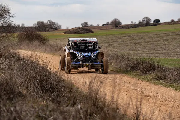 Maverick 'in engebeli off-road aracı açık araziler ve seyrek ağaçlarla çevrili toprak bir yolda hızla ilerliyor. Canlı manzara, arka planda parlak bir gökyüzü ve yuvarlanan tepeleri sergiliyor..
