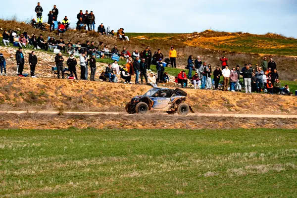 Resimli bir kırsal alanda Maverick olabilir miyim? Büyük bir kalabalık heyecan verici off-road yarışı izlemek için toplanıyor. Seyirciler, araçların toprak yollarda hızla ilerleyerek tozu kaldırmasına tezahürat ediyor.