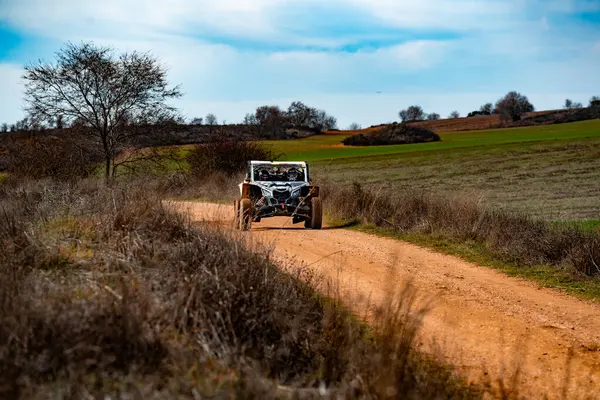 Yeşil ve seyrek ağaçlarla çevrili toprak bir yolda Maverick marka bir araç hızla gidebilir. Açık gökyüzü iyi havayı işaret ediyor, bu da onu off-road keşfi için ideal bir gün yapıyor..