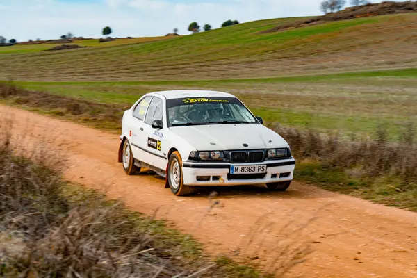 BMW serie 3 yarış arabası, açık mavi gökyüzünün altında yemyeşil çayırlarla çevrili toprak bir yolda yol alır. Doğadaki motor sporunun heyecanını gösterir..