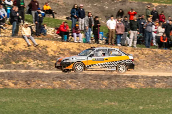 Hyunai Accent 'in ralli arabası toprak yolda hız yaparken, seyirciler heyecan verici motor sporunun tadını çıkarmak için yamaçta toplanıyor. Motorlar kükredikçe heyecan havayı dolduruyor..