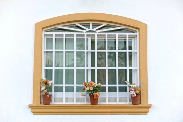 stock image Glass window decorated with flowers on the outside. Yellow framed window in white wall, view from outside.