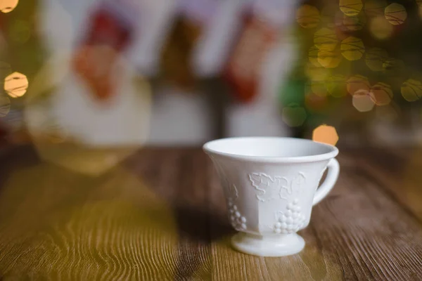 White tea cup with embossed engraving on wooden table with Christmas background.