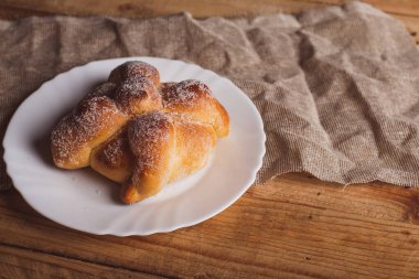 Pan de Muerto beyaz bir tabakta, ahşap bir masada izole halde. Tipik Meksika tatlıları..