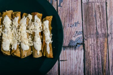 Tahta bir masada peynirli ve kremalı tacos flauta. Meksika atıştırmaları.