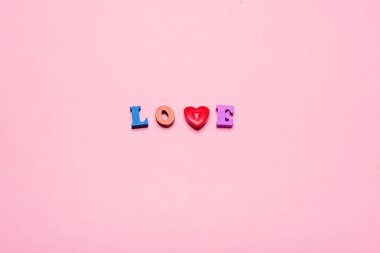 Aşk kelimesi ahşap harflerden ve pembe arka planda bir kalpten oluşur.