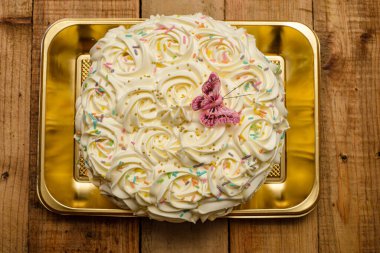 Kek, ahşap bir masada tereyağı kremalı çiçeklerle süslenmiş..