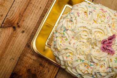 Kek, ahşap bir masada tereyağı kremalı çiçeklerle süslenmiş..