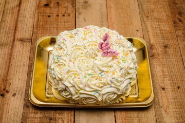 Kek, ahşap bir masada tereyağı kremalı çiçeklerle süslenmiş..