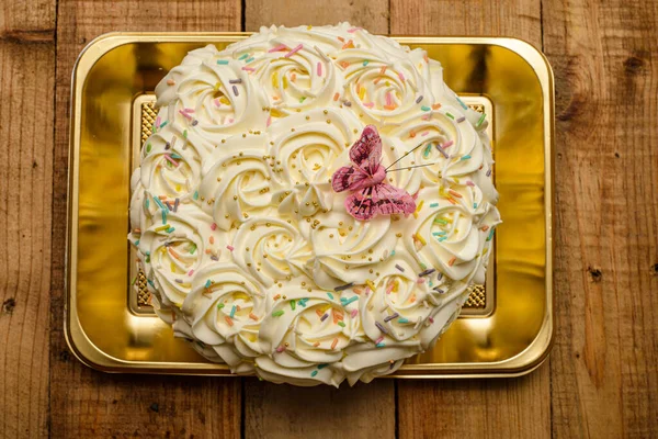 Kek, ahşap bir masada tereyağı kremalı çiçeklerle süslenmiş..