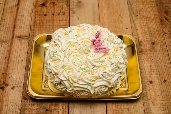 Kek, ahşap bir masada tereyağı kremalı çiçeklerle süslenmiş..