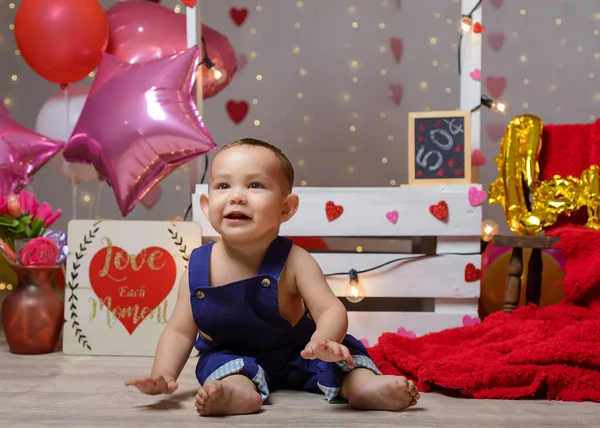 Portrait of a baby in a kissing booth decorated with hearts and balloons. Photo session celebrating the day of love and friendship.