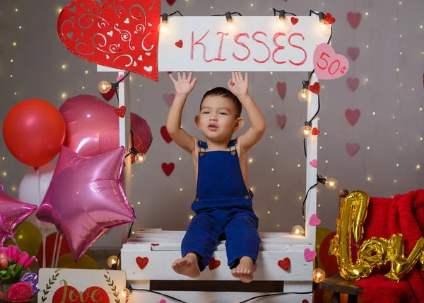 Portrait of a boy in a kissing booth decorated with hearts and balloons. Photo session celebrating the day of love and friendship.