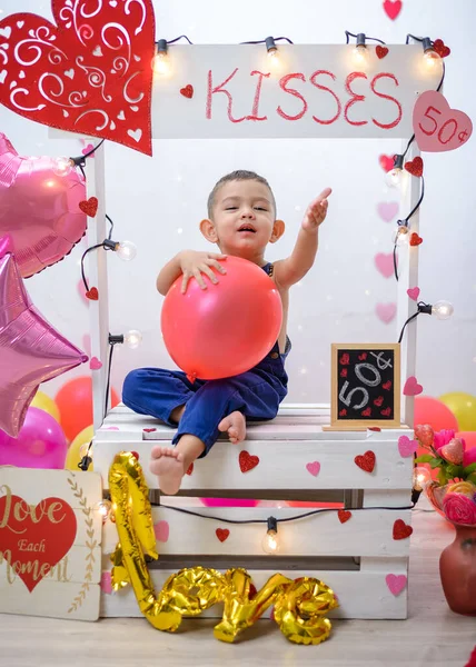 Portrait of a boy in a kissing booth decorated with hearts and balloons. Photo session celebrating the day of love and friendship.