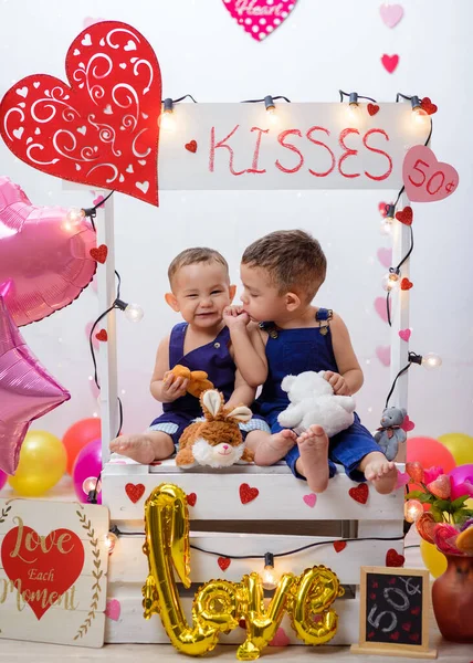 Portrait of two children in a kissing booth decorated with hearts and balloons. Photo session celebrating the day of love and friendship.