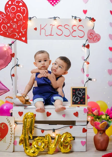 Portrait of two children in a kissing booth decorated with hearts and balloons. Photo session celebrating the day of love and friendship.