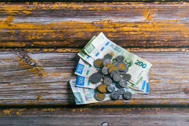 Stack of Mexican coins and bills on wooden table.