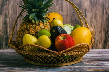 Basket with a group of different fruits on a wooden table. Wicker basket with ripe fruits.