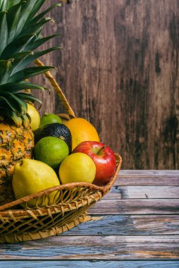 Basket with a group of different fruits on a wooden table. Wicker basket with ripe fruits.