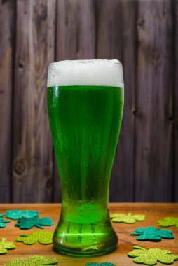 Glass of green beer on wooden table with glittering clovers.