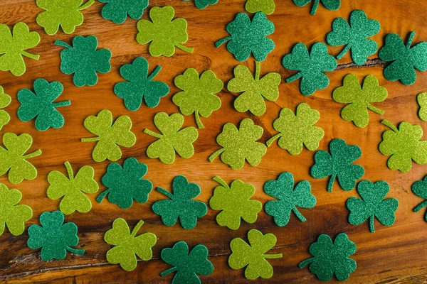 Three-leaf and four-leaf clover made of glitter material on wooden table. Saint Patrick\'s Day background.