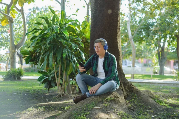 Šedovlasý Muž Který Poslouchá Hudbu Sluchátky Píše Svém Mobilu Sedí — Stock fotografie