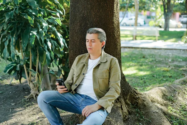 Šedovlasý Muž Který Poslouchá Hudbu Sluchátky Píše Svém Mobilu Sedí — Stock fotografie