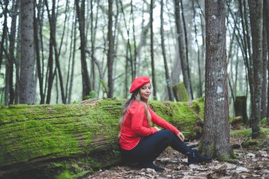 Ormanın ortasında yosunlu bir ağaç gövdesine yaslanmış gülümseyen kadın kameraya bakıyor..