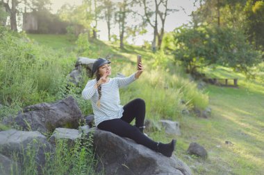 Doğanın ortasında bir kayanın üzerinde selfie çeken bir kadın..