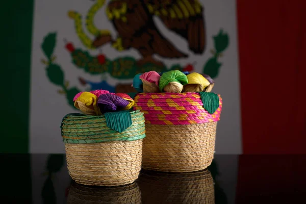 Small Mexican handmade baskets made with woven palm fiber. Handicrafts with Mexican flag in the background.