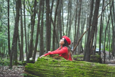 Ormanın ortasında yosunlu bir ağaç gövdesine yaslanmış gülümseyen kadın kameraya bakıyor..