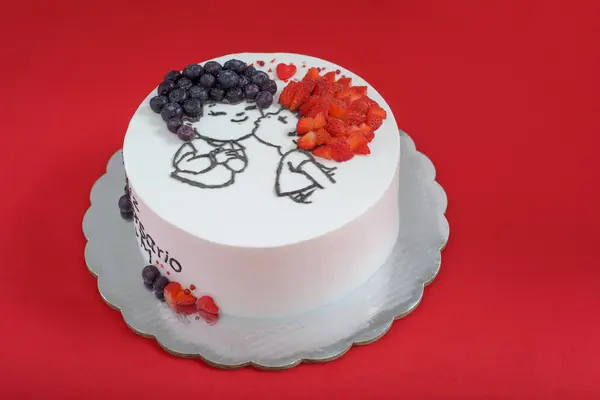 White cake decorated with drawing and red fruits. Beautiful white cake on red background.