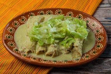 Ahşap bir masada kil tabakta servis edilen marullu yeşil Enchiladas..