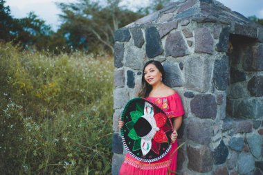 Geleneksel şapka ve elbise giyen Meksikalı kadın. Açık hava portresi taş duvarın yanında..