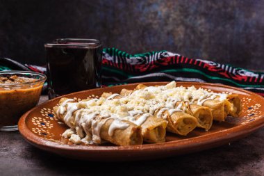 Meksika çamur tabaklarında kremalı ve peynirli kızarmış patates tacoları. Tacos dorados, Meksika yemeği..