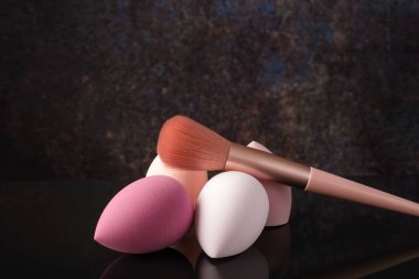 Siyah yansıtıcı arka planda makyaj için fırçalar ve süngerler.