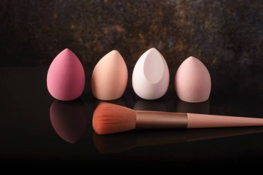 Siyah yansıtıcı arka planda makyaj için fırçalar ve süngerler.