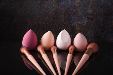 Siyah yansıtıcı arka planda makyaj için fırçalar ve süngerler.