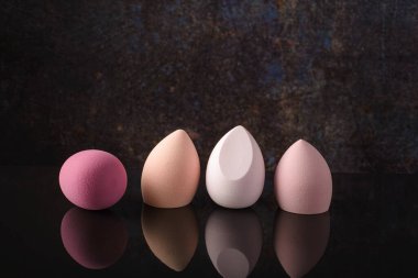 Siyah yansıtıcı arka planda makyaj için süngerler.