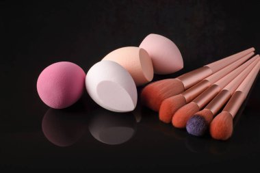 Siyah yansıtıcı arka planda makyaj için fırçalar ve süngerler.
