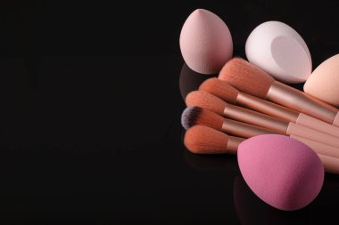 Siyah yansıtıcı arka planda makyaj için fırçalar ve süngerler.