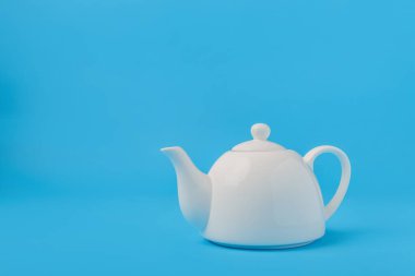 Mavi arkaplanda beyaz seramik çaydanlık izole.