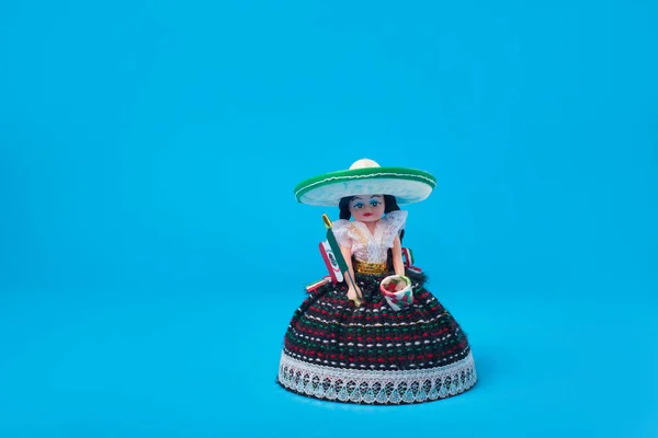 Small doll representing a Mexican woman with hat and Mexican flag. Isolated figure on blue background.